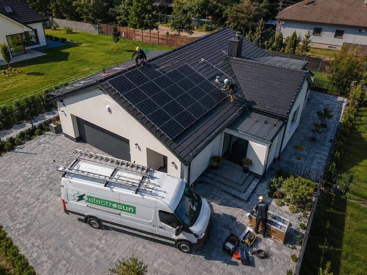 Montaj de panouri fotovoltaice pe acoperișul unei case, văzut de sus, cu o dubă de serviciu parcată în curte